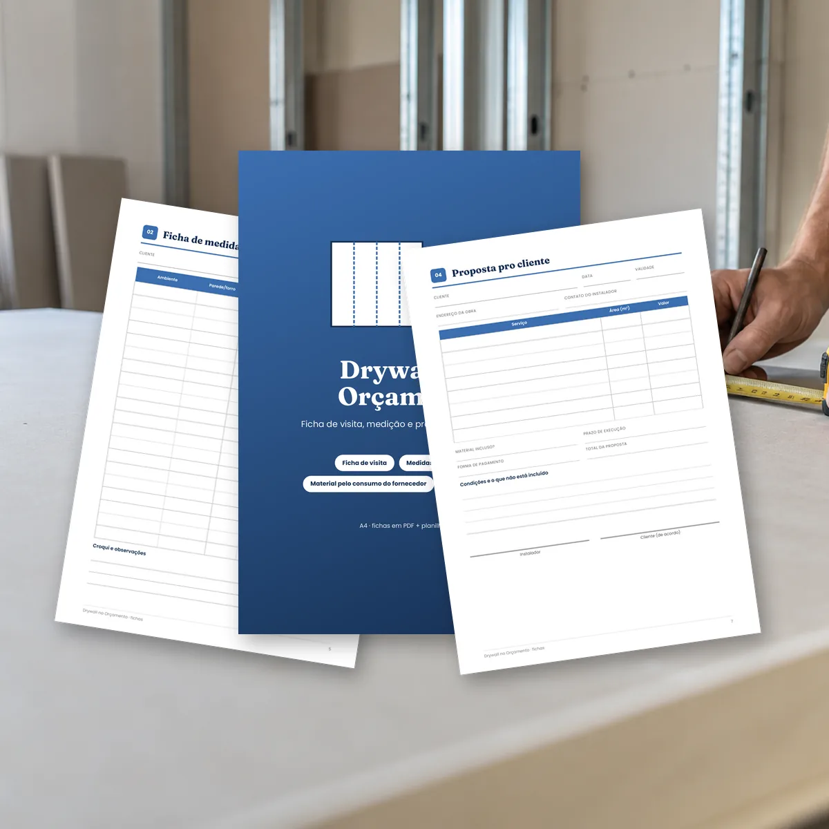 Fichas do Drywall no Orçamento sobre a bancada, com parede de drywall em montagem ao fundo. Montagem com páginas reais do PDF.